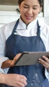 Köchin im weißen Arbeitskittel dokumentiert Küchenabläufe auf einem Tablet
