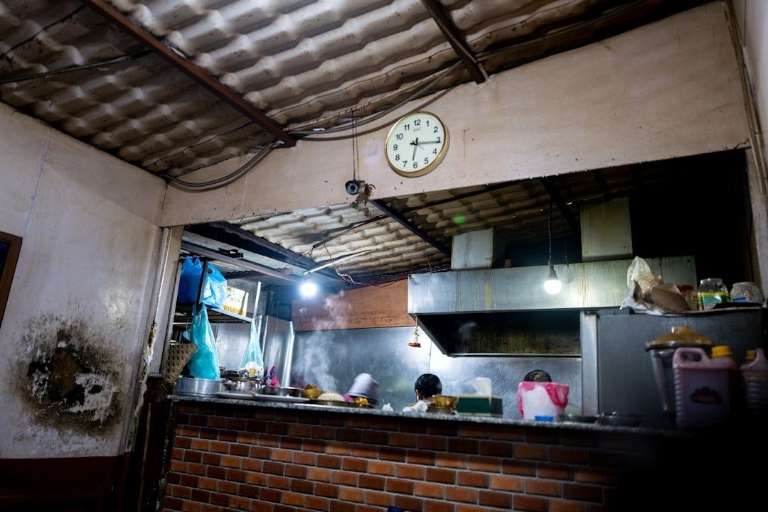 Einfache Restaurantküche mit Wanduhr, Herdabzug und sichtbarem Küchenpersonal